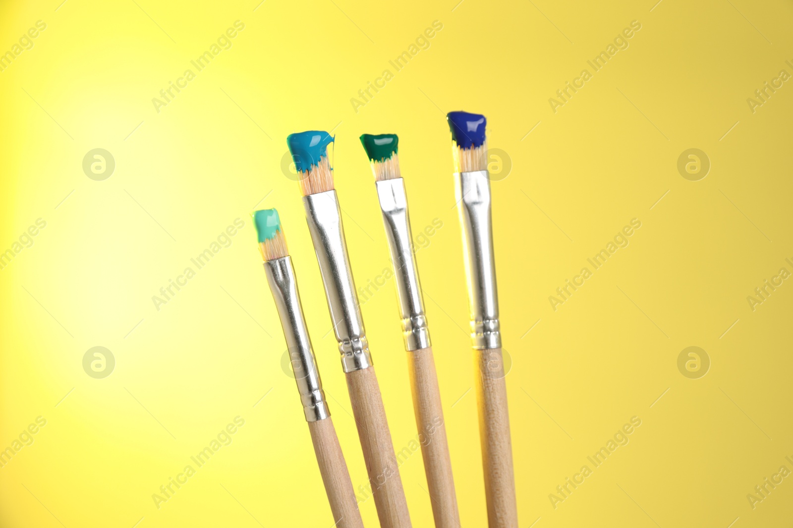 Many brushes with color paints on yellow background, closeup Photo of Many brushes with color paints on yellow background, closeup