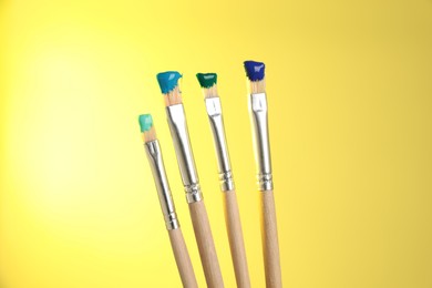 Photo of Many brushes with color paints on yellow background, closeup