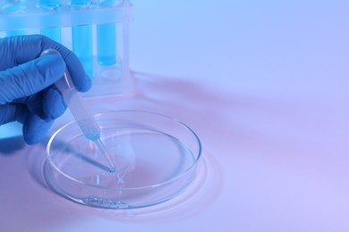 Photo of Scientist taking sample with pipette out of Petri dish on light background, closeup. Space for text