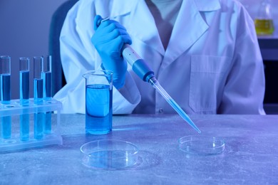 Photo of Scientist taking sample with micropipette out of Petri dish at table in laboratory, closeup