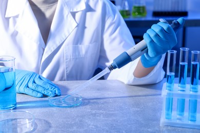 Photo of Scientist taking sample with micropipette out of Petri dish at table in laboratory, closeup