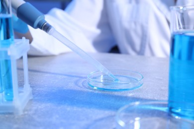 Photo of Scientist taking sample with micropipette out of Petri dish at table in laboratory, closeup