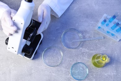 Photo of Scientist working with microscope and Petri dishes at table, top view