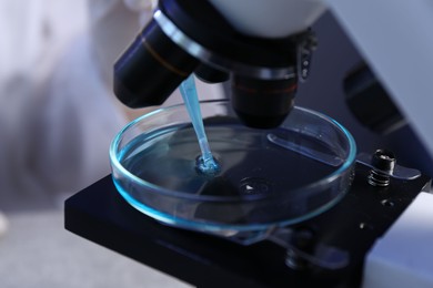 Photo of Dripping liquid with pipette onto Petri dish on microscope in laboratory, closeup