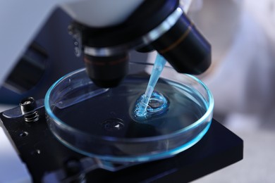 Photo of Dripping liquid with pipette onto Petri dish on microscope in laboratory, closeup