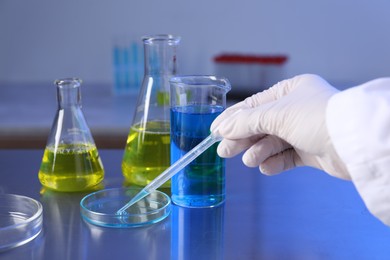 Photo of Scientist taking sample with pipette out of Petri dish at table in laboratory, closeup
