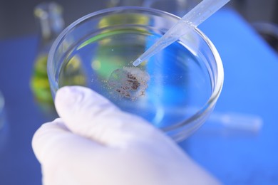 Photo of Scientist dripping liquid with pipette onto Petri dish in laboratory, closeup