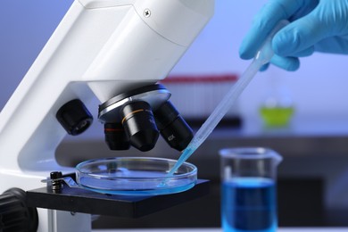 Photo of Scientist dripping liquid with pipette onto Petri dish on microscope in laboratory, closeup