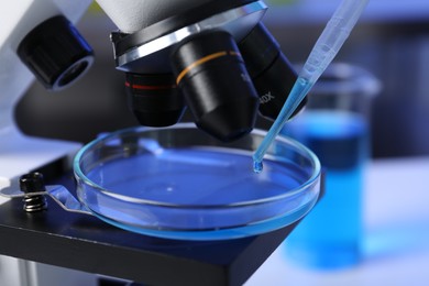 Photo of Dripping liquid with pipette onto Petri dish on microscope in laboratory, closeup