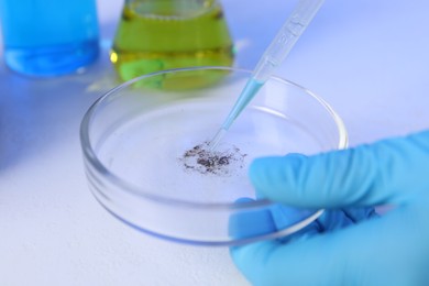 Photo of Scientist dripping liquid with pipette onto Petri dish on white background, closeup