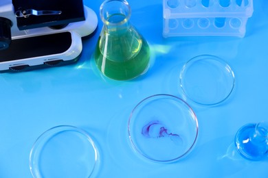 Photo of Petri dishes and flasks with samples on light blue background, above view