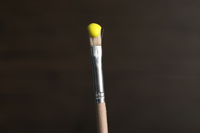 Photo of Brush with yellow paint on wooden background, closeup