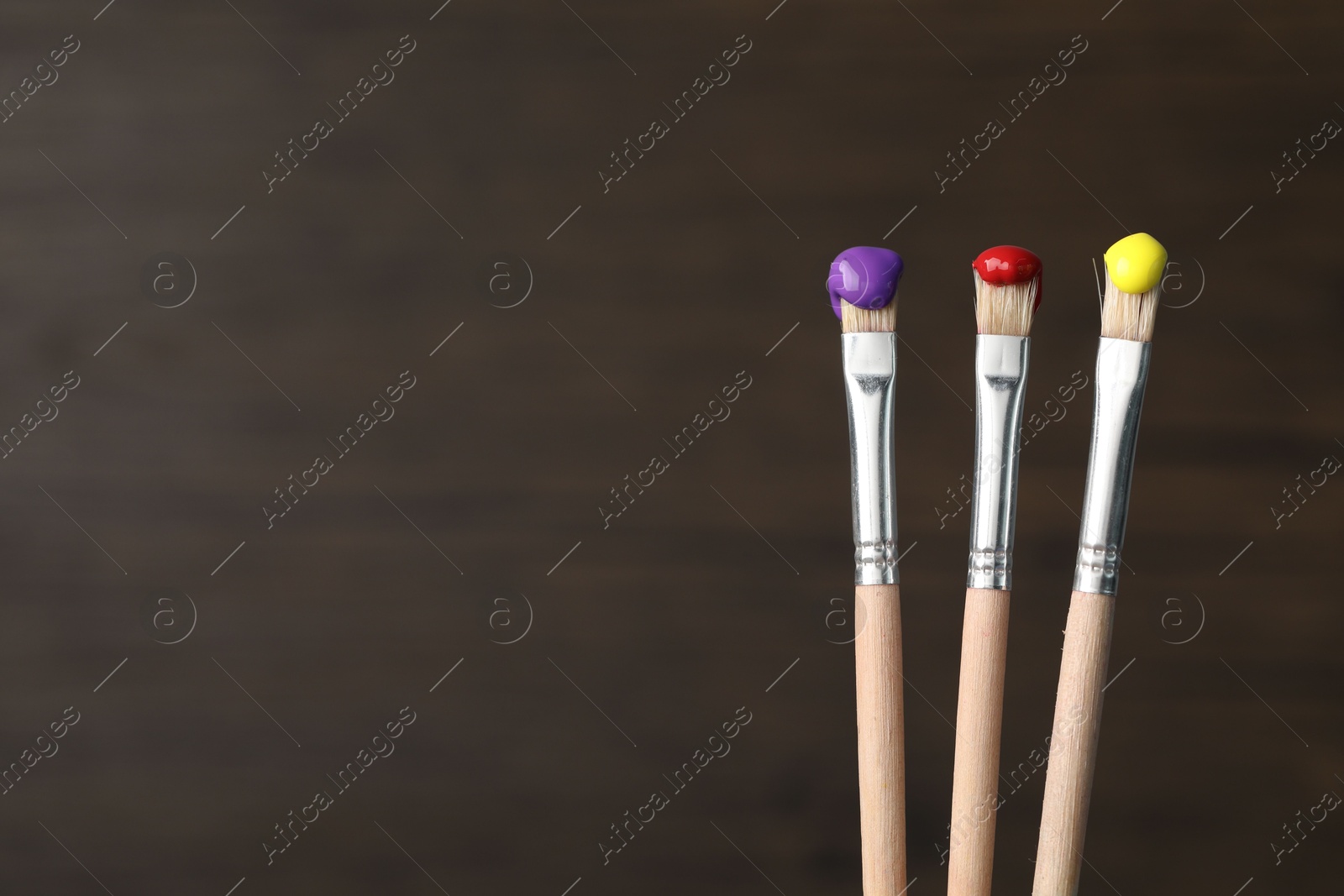Three brushes with color paints on wooden background, closeup. Space for text Photo of Three brushes with color paints on wooden background, closeup. Space for text