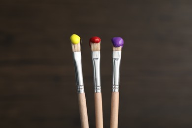 Photo of Three brushes with color paints on wooden background, closeup