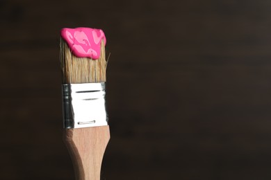 Photo of Brush with pink paint on wooden background, closeup. Space for text