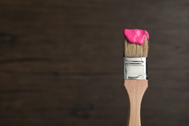 Photo of Brush with pink paint on wooden background, closeup. Space for text