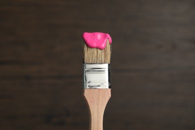 Photo of Brush with pink paint on wooden background, closeup