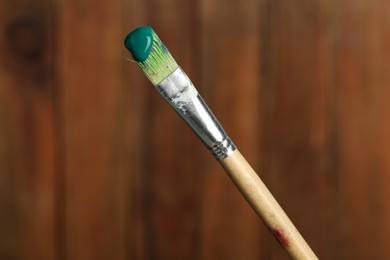 Photo of Brush with green paint on wooden background, closeup