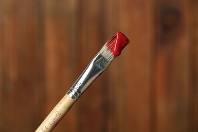 Photo of Brush with red paint on wooden background, closeup