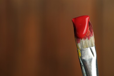 Photo of Brush with red paint on wooden background, closeup. Space for text