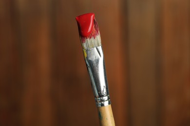 Photo of Brush with red paint on wooden background, closeup