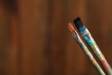Photo of Two dirty paintbrushes on wooden background, closeup. Space for text