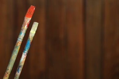 Photo of Two dirty paintbrushes on wooden background, closeup. Space for text