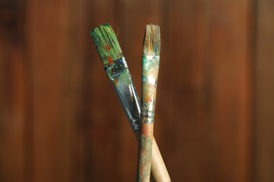 Photo of Two dirty paintbrushes on wooden background, closeup