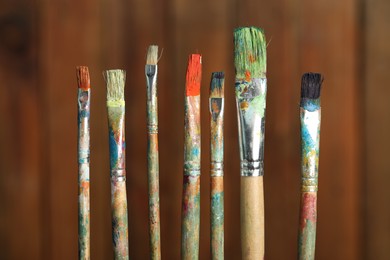 Photo of Many dirty paintbrushes on wooden background, closeup