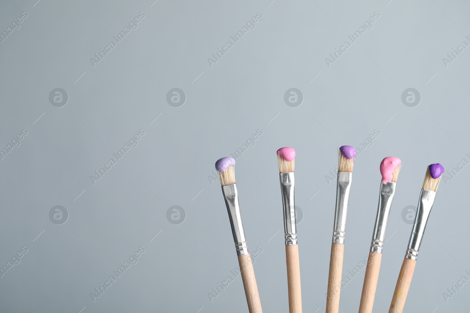 Many brushes with color paints on light grey background, closeup. Space for text Photo of Many brushes with color paints on light grey background, closeup. Space for text