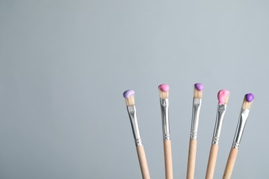Photo of Many brushes with color paints on light grey background, closeup. Space for text