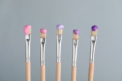 Photo of Many brushes with color paints on light grey background, closeup