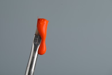 Photo of Brush with orange paint on light grey background, closeup. Space for text
