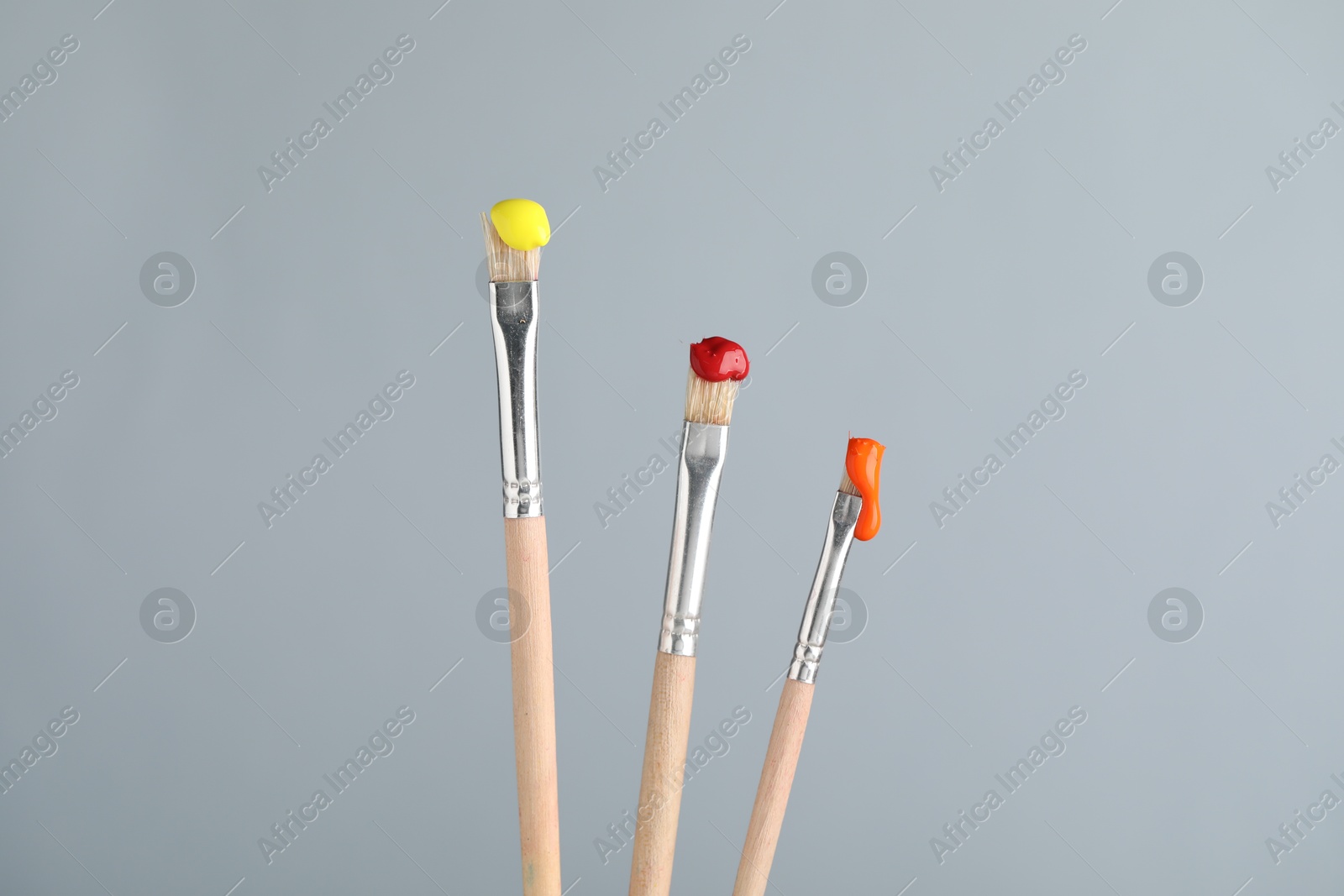 Three brushes with color paints on light grey background, closeup Photo of Three brushes with color paints on light grey background, closeup
