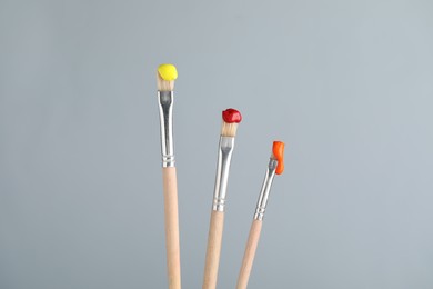 Photo of Three brushes with color paints on light grey background, closeup