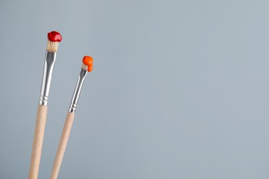 Photo of Two brushes with color paints on light grey background, closeup. Space for text