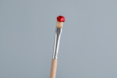 Photo of Brush with red paint on light grey background, closeup