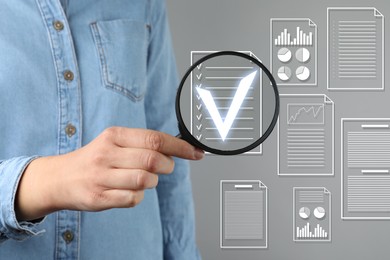 Image of Woman holding magnifying glass over virtual approved document with check mark against grey background, closeup