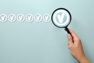 Image of Approved. Woman holding magnifying glass over check mark on light blue background, top view