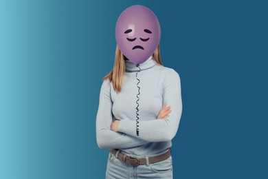 Image of Balloon with sad face in front of woman's head on blue background