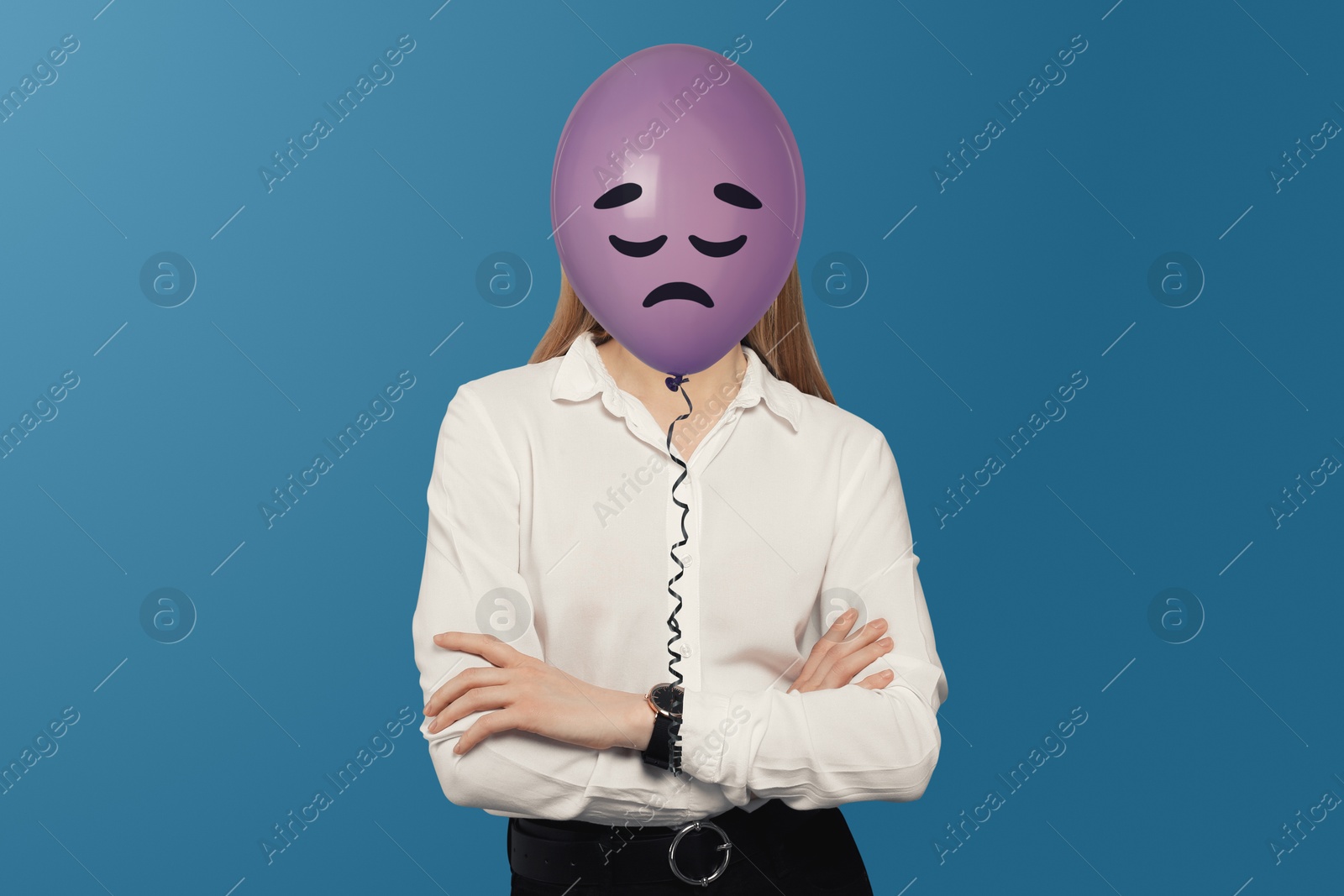 Woman hiding behind violet balloon with sad face on blue background Image of Woman hiding behind violet balloon with sad face on blue background