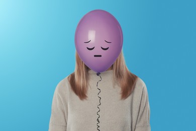 Image of Woman hiding behind violet balloon with sad face on light blue background