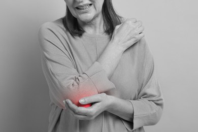 Image of Arthritis. Senior woman suffering from pain in elbow, closeup. Black and white toning with red color accent