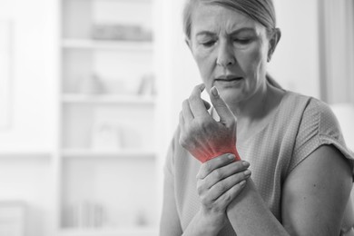 Image of Arthritis. Senior woman suffering from wrist pain indoors. Black and white toning with red color accent