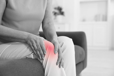 Image of Arthritis. Woman suffering from knee pain on sofa at home, closeup. Black and white toning with red color accent