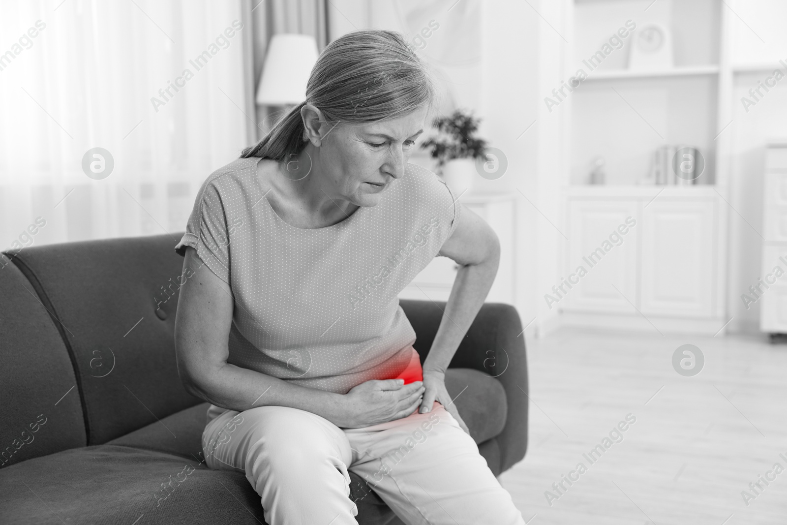 Arthritis. Senior woman suffering from hip joint pain on sofa at home. Black and white toning with red color accent Image of Arthritis. Senior woman suffering from hip joint pain on sofa at home. Black and white toning with red color accent