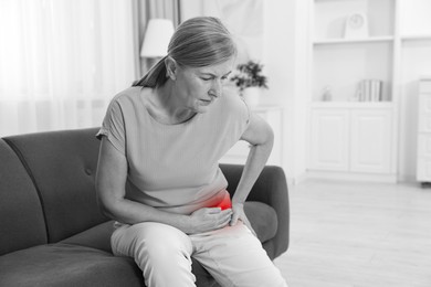 Image of Arthritis. Senior woman suffering from hip joint pain on sofa at home. Black and white toning with red color accent