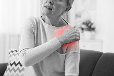 Image of Arthritis. Senior woman suffering from pain in shoulder at home, closeup. Black and white toning with red color accent