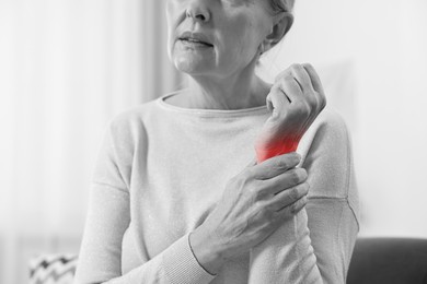 Image of Arthritis. Senior woman suffering from wrist pain indoors, closeup. Black and white toning with red color accent