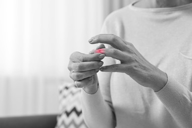 Image of Arthritis. Woman suffering from pain in finger at home, closeup. Black and white toning with red color accent